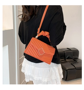 Detail of orange quilted crossbody bag with golden buckle and stylish ruched handle