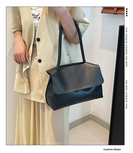 Detail of a large black leather tote bag with a minimalist flap worn by a model in a suit