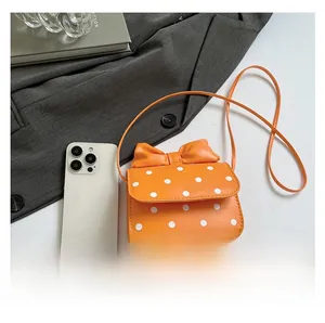 Detailed comparison of orange polka dot mini bag with bow accent and smartphone