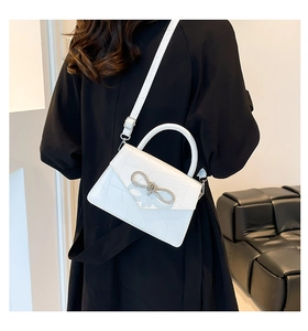 Close-up of white croc-effect crossbody bag with a sparkling rhinestone bow buckle detail