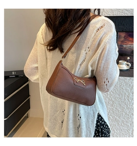 Brown lychee leather underarm bag with gold bow clasp shown on model shoulder