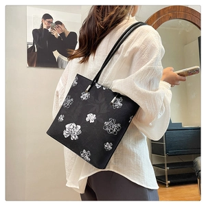 Detailed close-up of black tote bag featuring floral print and silver metal connectors