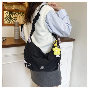 Detail of black canvas bag featuring pink drawstring bows and pleated shoulder strap