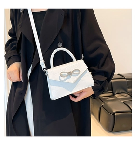 Close-up of white crocodile pattern leather bag with sparkling diamond bow metal clasp
