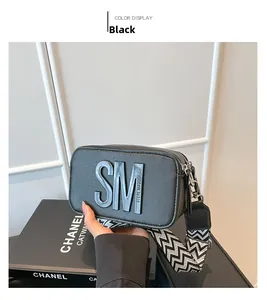 Détail du sac caméra en cuir noir avec large bandoulière géométrique et logo en relief