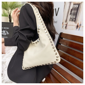 Detail shot of cream leather underarm bag with silver studs on a model in urban setting