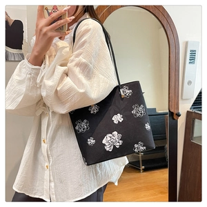 Detail of a black tote bag featuring delicate white floral embroidery and metallic strap buckles