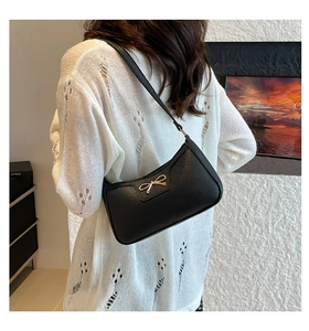 Detail of black pebbled leather baguette bag with a golden bow buckle on model back