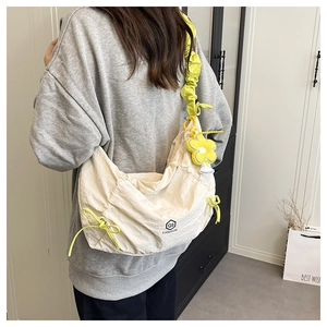Detail of cream oversized crossbody bag with neon yellow drawstrings and flower charm