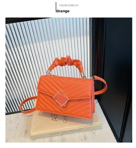 Close-up of quilted orange leather handbag featuring a stylish square metal lock clasp