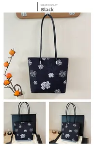 Detail view of black tote bag with white floral pattern and silver hardware in gift box