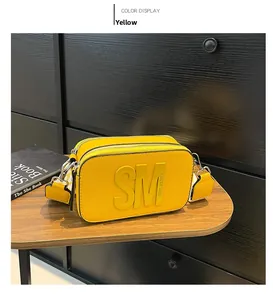 Détail de sac bandoulière en cuir jaune avec logo gaufré et fermetures éclair en métal