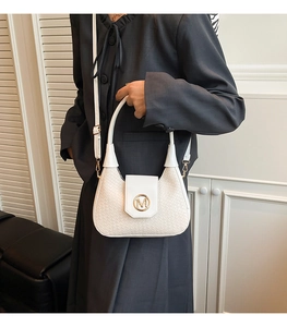Detalle de bolso de media luna blanco trenzado con logo M dorado y blazer gris