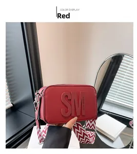Détail d'un sac à bandoulière rouge en cuir croisé avec une large sangle tissée bicolore