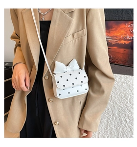 Detailed view of white polka dot crossbody bag with large decorative bow on the flap