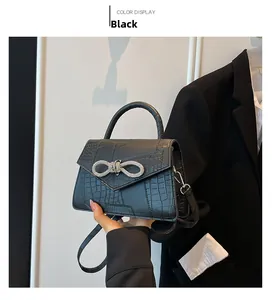 Detail of black faux crocodile leather handbag featuring a sparkling rhinestone bow buckle