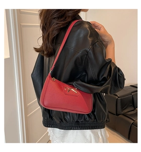 Detail of red baguette bag with lychee texture and golden metal bow decoration