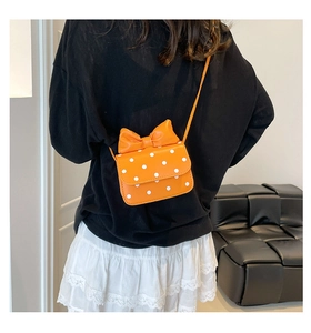 Detail view of mini orange polka dot crossbody bag with a large bow shown on a female model