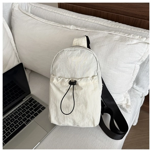 Lightweight cream nylon crossbody bag with adjustable strap next to a laptop