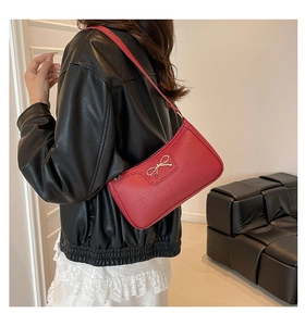 Detail of red bow shoulder bag featuring lychee texture and gold metallic hardware accents