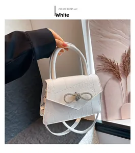 Close-up of white crocodile pattern handbag with sparkling diamond bow buckle detail
