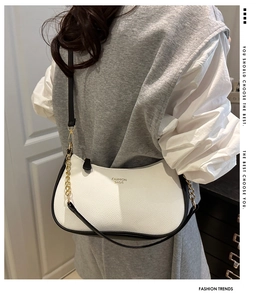 Close-up of textured white leather underarm bag with gold chain and black strap detail