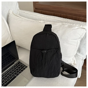 Detail of black nylon crossbody bag with drawstring pocket on a soft white cushion