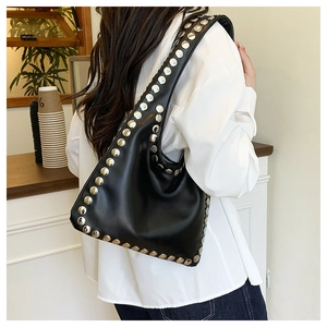 Detail of a black hobo bag with silver rivets shown on a shoulder in a modern cafe setting