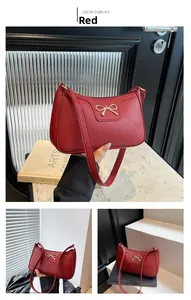 Close-up of red baguette shoulder bag with lychee texture and gold bow detail