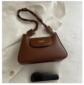 Brown leather handbag with metal bow detail and woven strap next to a mobile phone