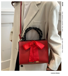 Detail of red leather crossbody bag with a large silk bow worn by a model in beige suit