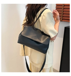 Side view of black leather tote bag with flap closure on model in minimalist room