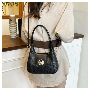 Detail of black woven leather texture bag featuring a gold M logo buckle and sturdy top handle
