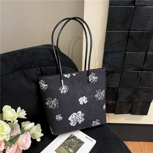 Large black tote bag with white floral prints and dual shoulder straps on a chair