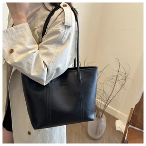 Dettaglio della borsa tote nera minimalista con trama litchi e spalline sottili su un trench