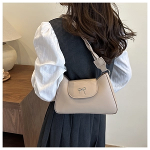 Chic beige shoulder bag with silver bow detail shown on model in a cozy interior