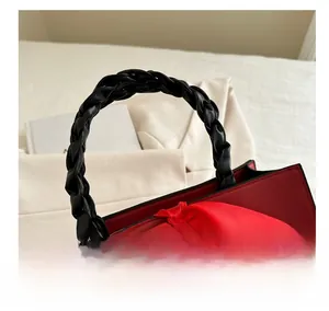 Detail of red leather handbag with black braided handles and large ribbed bow decoration