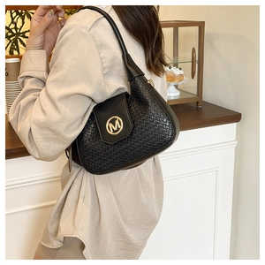 Detalle de bolso bandolera trenzado negro con hebilla circular de metal dorado logo M