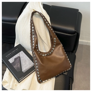 Detailed view of caramel leather hobo bag with vintage silver rivets on a leather sofa