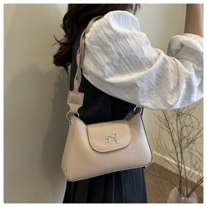 Detail of apricot shoulder bag with metallic bow and braided strap on model