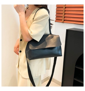 Close-up of black matte leather tote bag with large flap and long strap on model