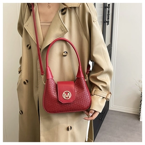 Detalle de bolso trenzado color granate con logo M dorado y herrajes metálicos