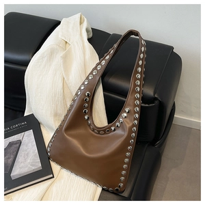 Close-up of caramel leather tote bag featuring stylish silver studs on a black sofa