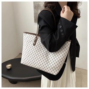 Detail shot of the cream tote bag showing brown monogram texture and gold rivets