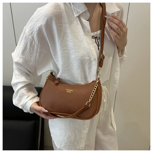 Brown lychee leather half-moon crossbody bag with gold chain worn by a model