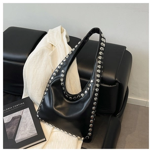 Close-up of black rivet tote bag with silver studs on a premium leather sofa background