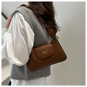 Detail of a brown leather shoulder bag with a silver metal bow and twisted woven strap