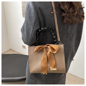 Brown leather square bag with black woven handle and silk bow shown on a shoulder