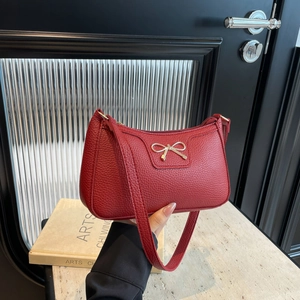 Red pebbled leather hobo shoulder bag with a gold bow accent held by a person