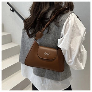 Detailed close-up of brown shoulder bag with silver metallic bow and smooth leather texture